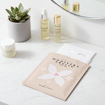 Korean Hydrating Sheet Mask pack with a light pink floral design, positioned beside skincare products on a marble surface.